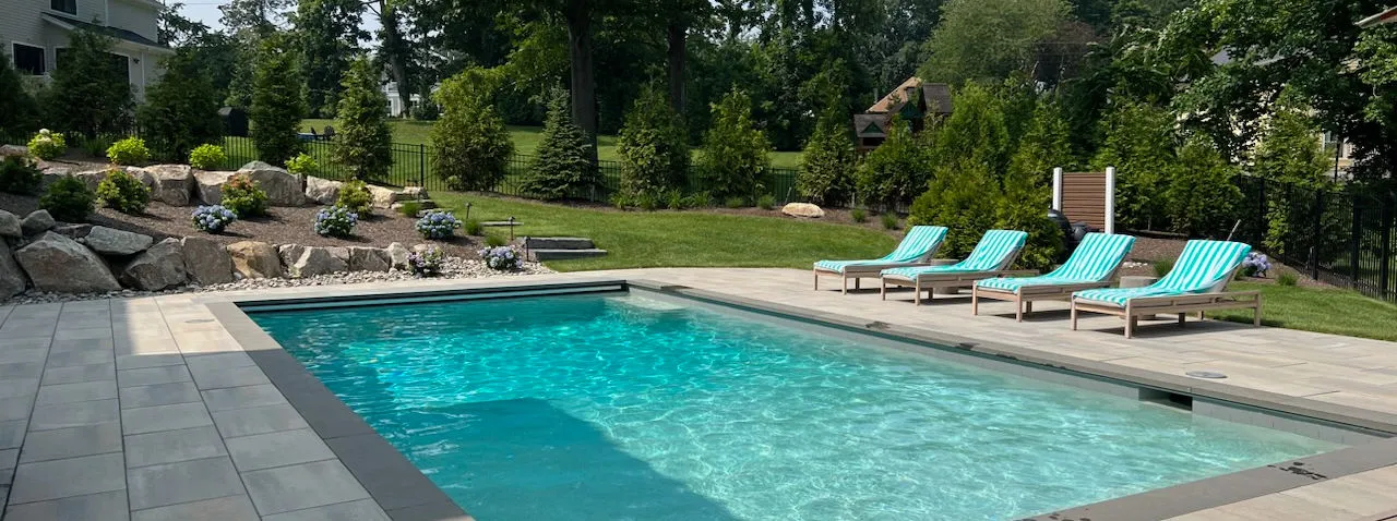 Inground pool with stone patio, lounge chairs and boulder plantings