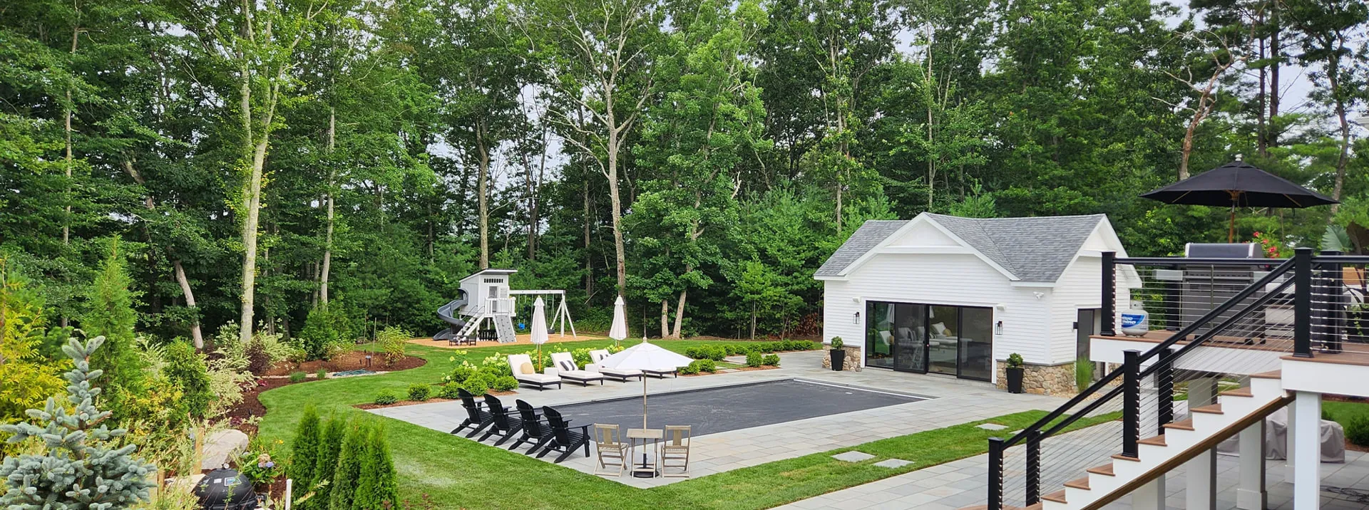 Backyard landscape with lawn, pool and pool house surrounded by trees